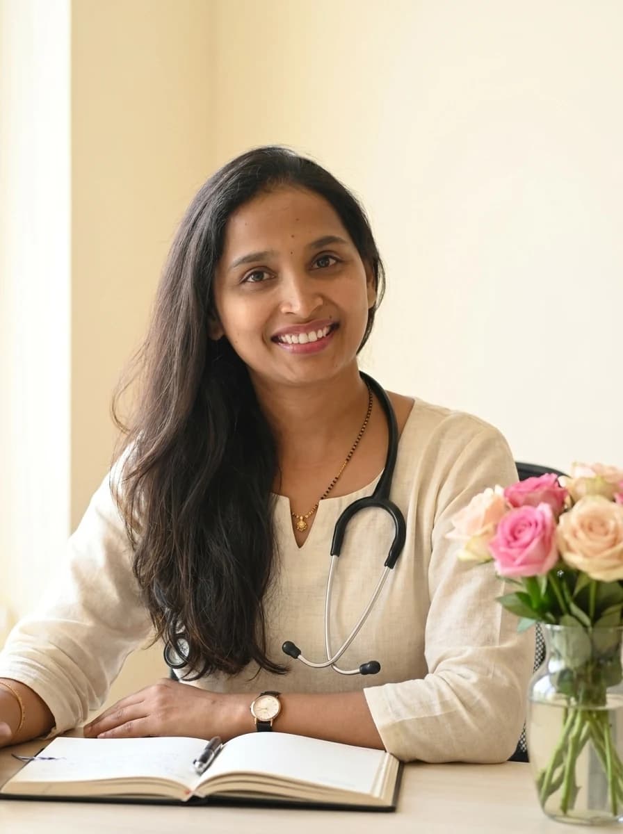 Dr. Geeta Kadamanahalli smiling at her desk, with a stethoscope, an open notebook and pink roses